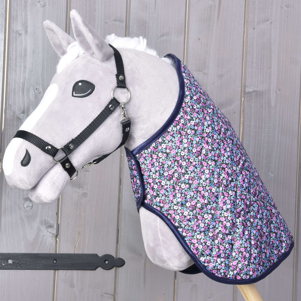 Siv Hobby Horse konj s črno oglavko, oblečen v prešito pregrinjalo s cvetličnim potiskom in temno modro obrobo čez vrat