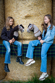 Dve deklici na balah slame, pokritih z zeleno škotsko karirasto odejo, vsaka drži sivega Hobby Horse konja z rjavo oglavko