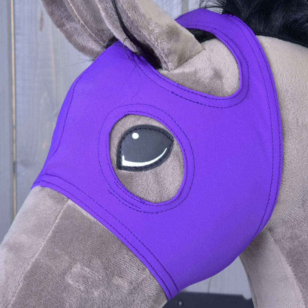 Bližnji posnetek vijolične maske na sivo rjavem Hobby Horse konju z ušesom, ki gleda skozi odprtino, in obšito odprtino za oko