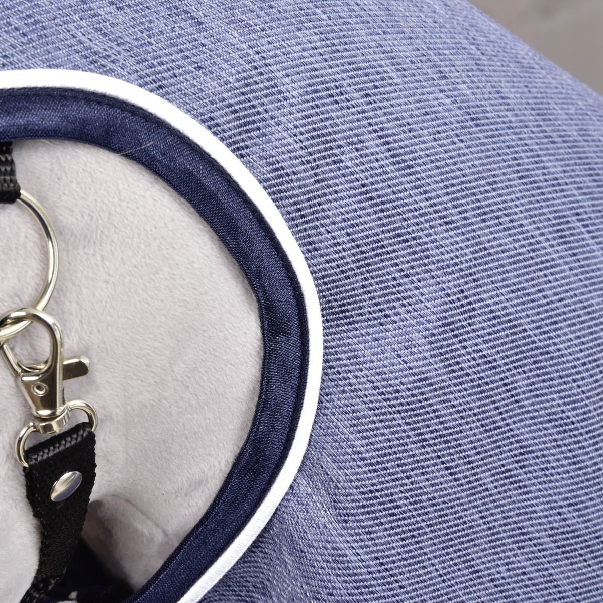 Close-up of the Raincoat Jeans: denim-textured blue fabric with navy binding and white piping at the neck opening