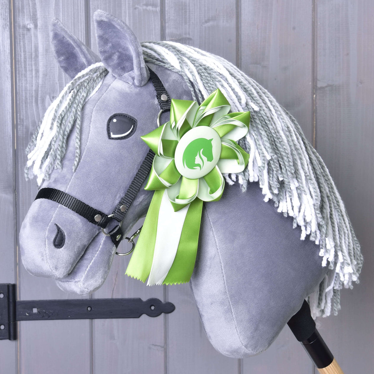 Siv plišast Hobby Horse konj s sivo-belo grivo iz preje in črno oglavko, zelena rozeta je pripeta na vrat