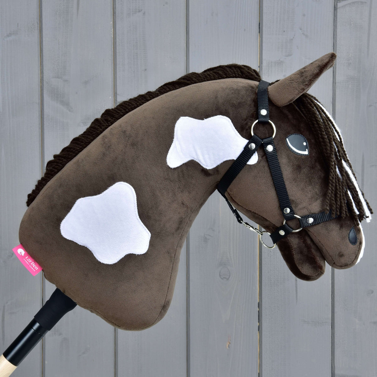 Hobby Horse Monte with Black Halter facing right, white patches on the brown neck and a pink LarDen label near the stick