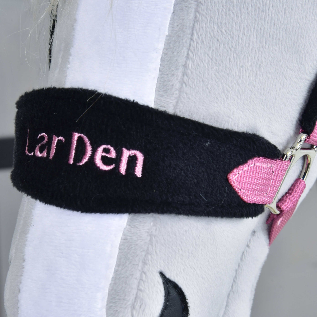 Close-up of the black fur noseband with LarDen embroidered in pink, on a light grey Hobby Horse with a white blaze