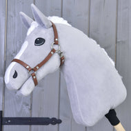 Siv plišast Hobby Horse konj z belo grivo in liso nosi rjavo oglavko iz umetnega usnja, pred sivo leseno steno