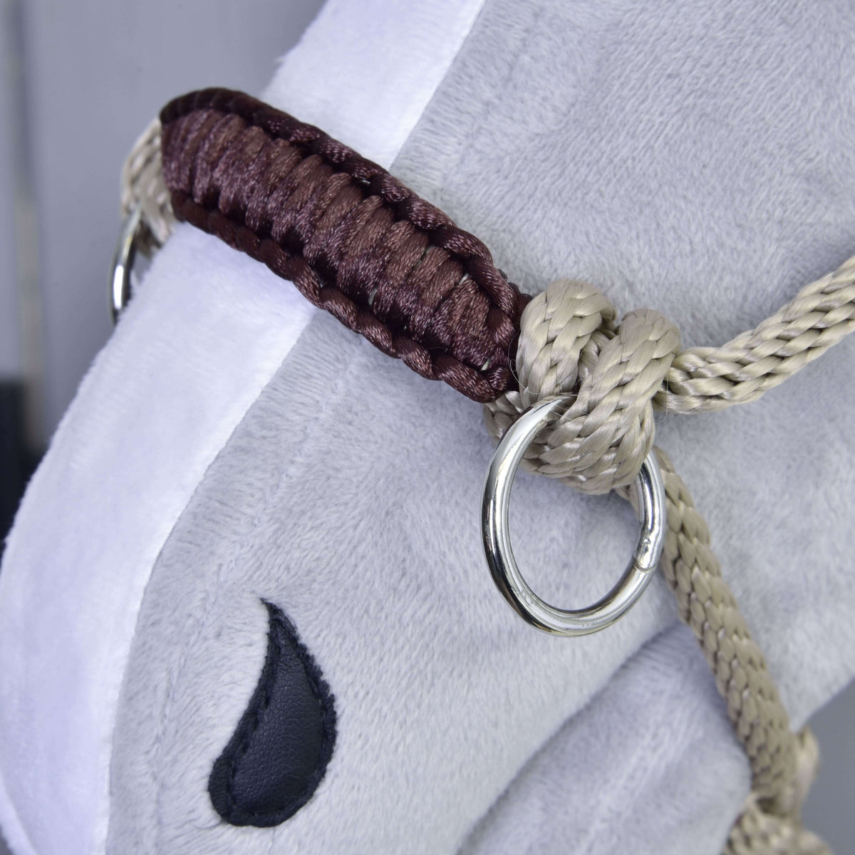 Close-up of the beige rope halter with its brown braided noseband and silver ring on a grey plush Hobby Horse