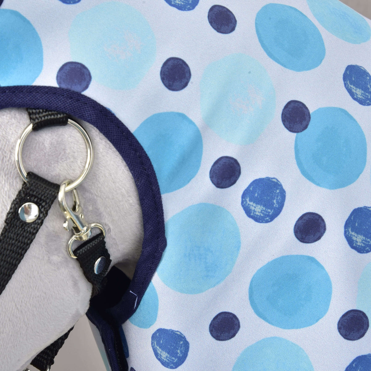 Close-up of the Raincoat Bubbles print, light blue and navy dots with navy binding at the neck beside a black halter clip