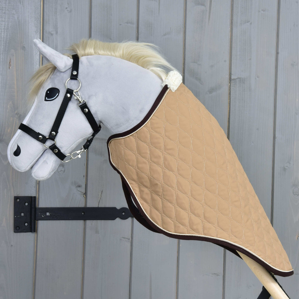Side view of the beige quilted travel rug on a grey plush Hobby Horse, covering the neck down to the wooden stick