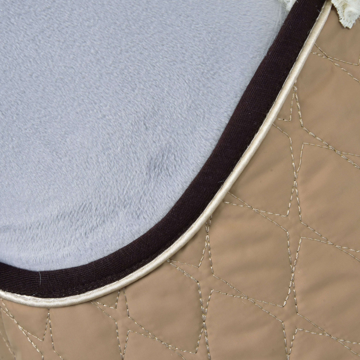 Close-up of the star-pattern quilting on the beige fabric with dark brown binding and cream piping against grey plush