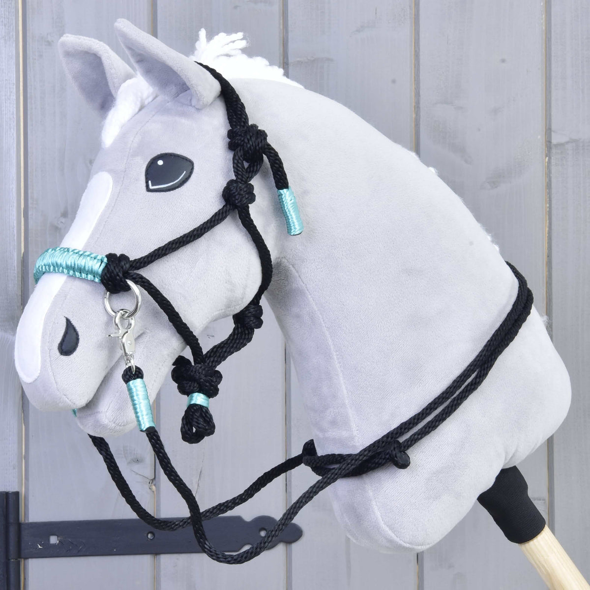 Grey Hobby Horse wearing the black rope halter with knots and turquoise wraps, with matching black reins over the neck
