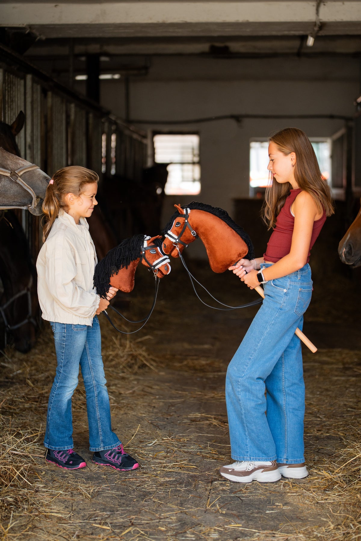 Dve deklici v hlevskem hodniku, vsaka drži Hobby Horse konja lisjaka s črno grivo in črno uzdo z belim oblazinjenjem