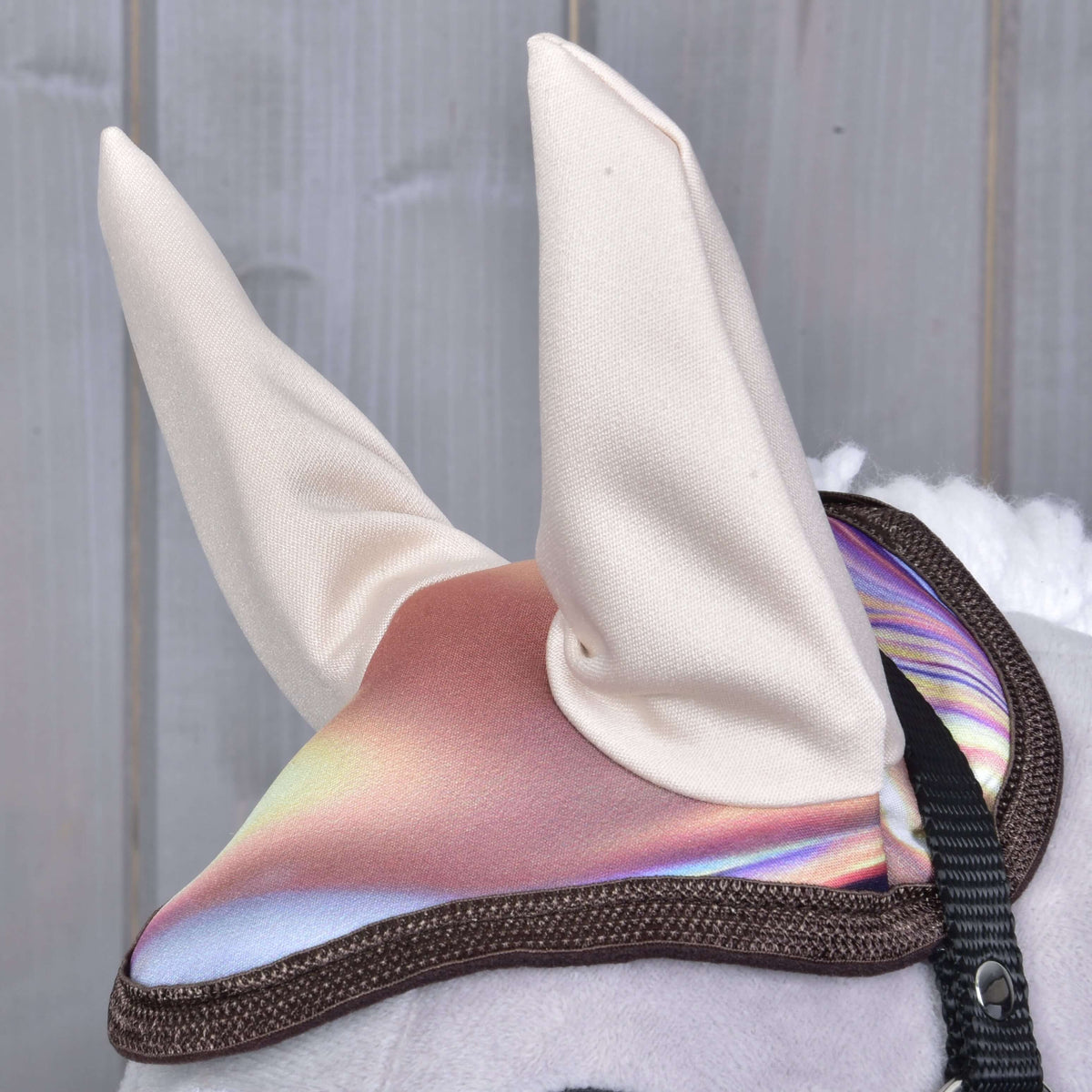 Close-up of the ear bonnet with tall cream ears and a shimmering pink and lilac crown edged in brown on a grey Hobby Horse
