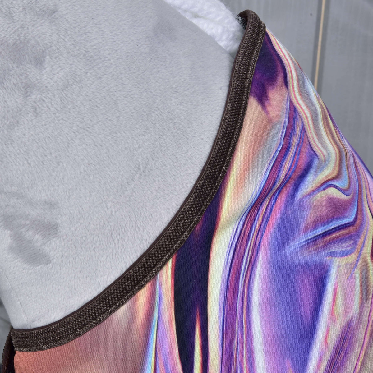 Close-up of the iridescent purple and pink blanket fabric with brown binding along the neck of a grey Hobby Horse