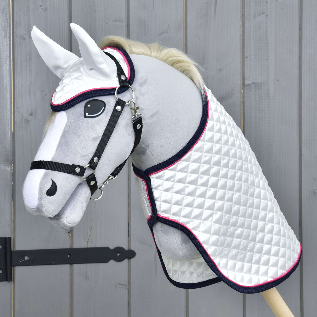 Grey plush Hobby Horse in a black halter wearing the white quilted satin blanket and ear bonnet with navy and pink trim