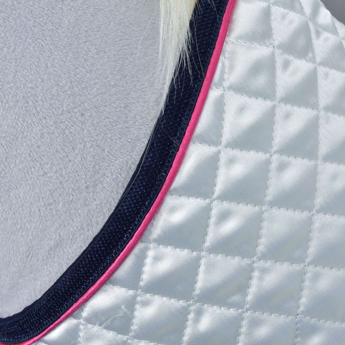 Close-up of the diamond-quilted white satin with pink piping and navy binding along the neckline of the blanket