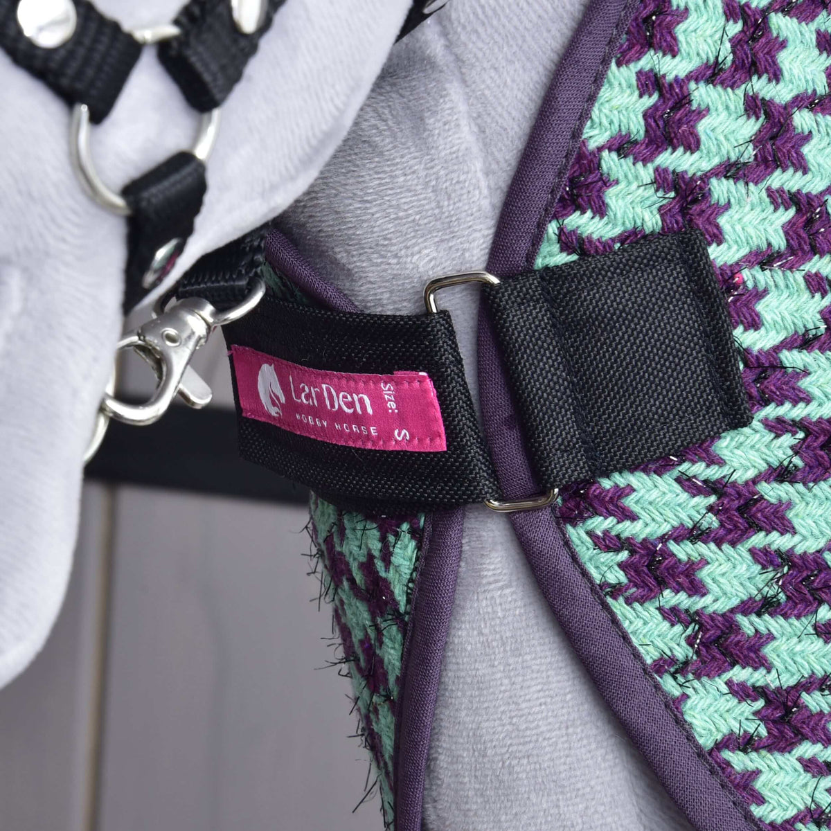 Chest strap of the Hobby Horse Stable Blanket Green closed with D-rings on a grey plush chest, pink LarDen label visible