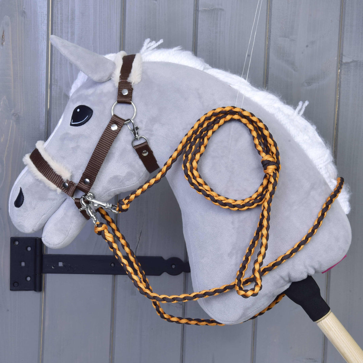 Svetlo siv Hobby Horse konj z rjavo oglavko z bež krznom ter pletenimi vajetmi in povodcem v oranžni in rjavi barvi