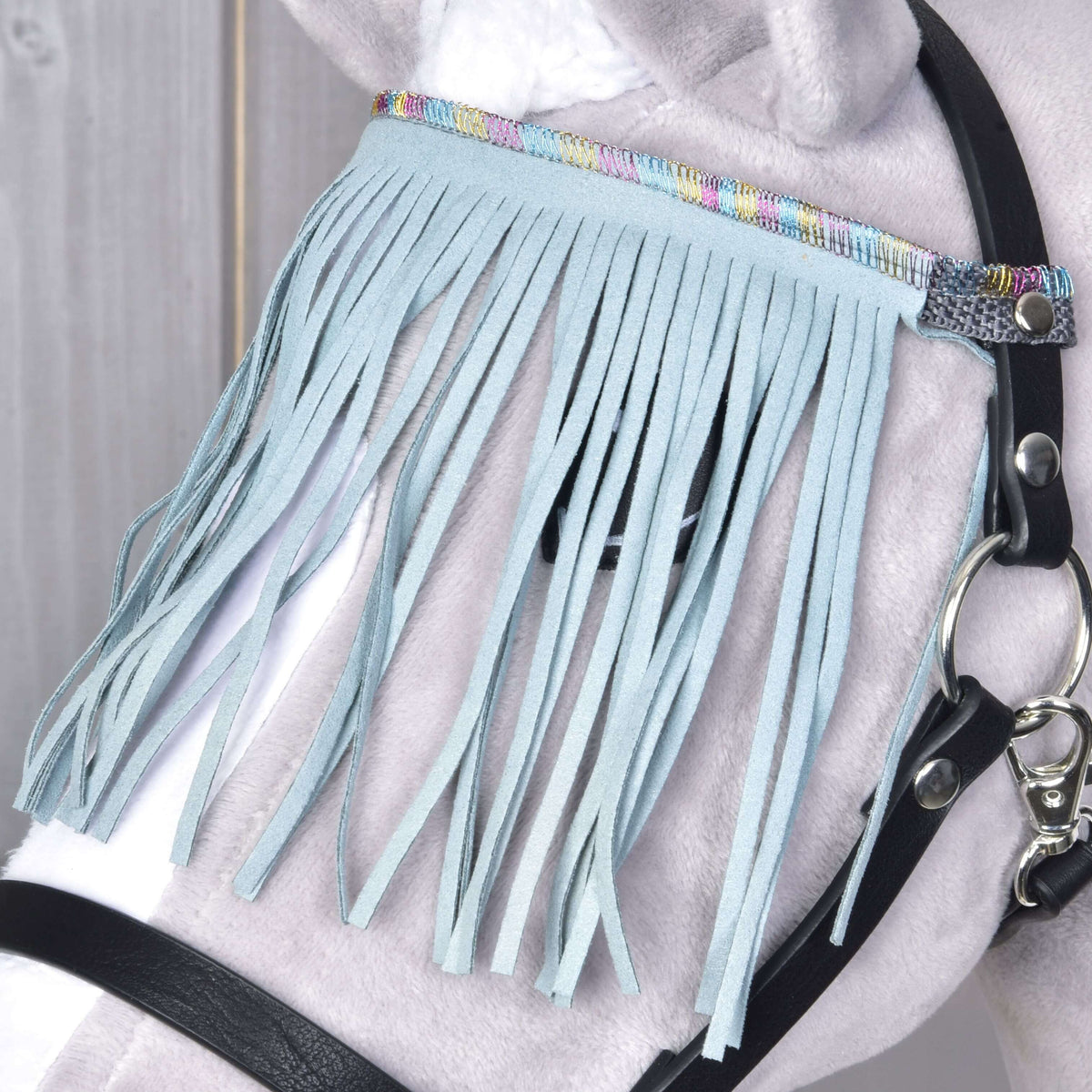 Bližnji posnetek bledo turkiznih res in pastelnega mavričnega traku ob srebrnem karabinu na sivem Hobby Horse konju