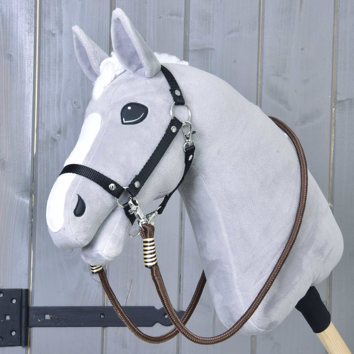 Svetlo siv Hobby Horse konj s črno oglavko in rjavimi vajetmi Vivaldi, pripetimi pod brado in speljanimi okoli vratu