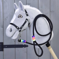 Siv plišast Hobby Horse konj s črno oglavko, črn povodec z mavričnimi ovoji je pripet pod brado in zvit ob njem