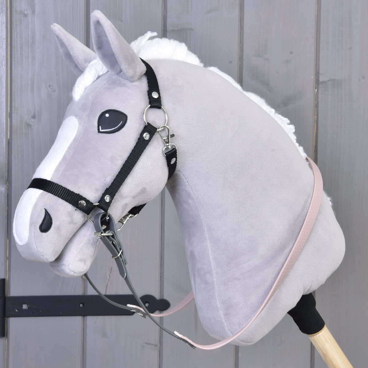 Grey plush Hobby Horse with a black halter and the rubberized dark grey and pale pink reins buckled to its rings