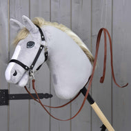 Svetlo siv Hobby Horse konj s črno oglavko in nanjo pripetimi deljenimi western vajetmi Dark Brown ob sivih lesenih vratih