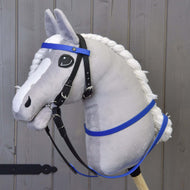 Siv plišast Hobby Horse konj v črni uzdi z modrim čelnikom in z modrimi gumiranimi vajetmi, siva lesena stena