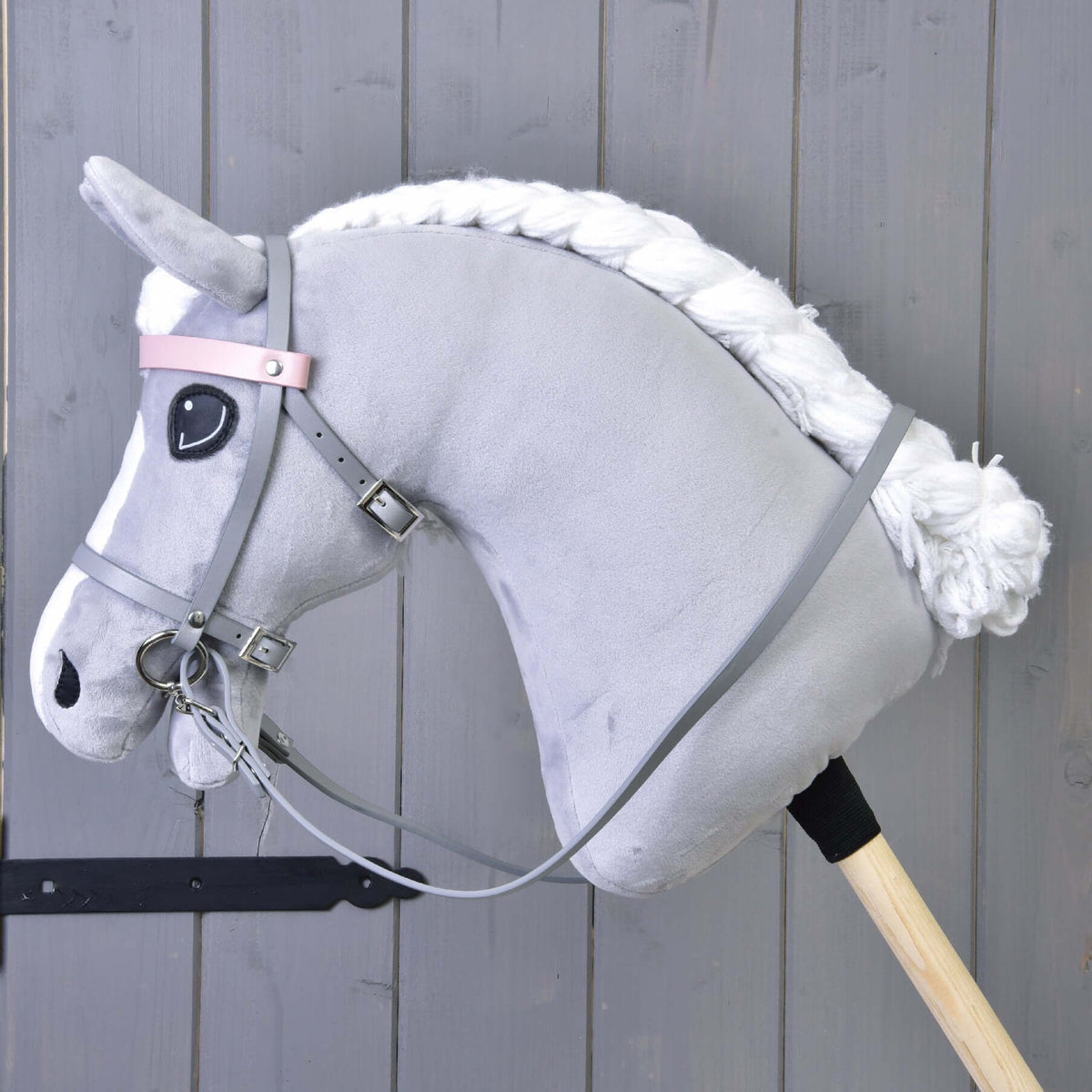 Siv plišast Hobby Horse konj s spleteno belo grivo nosi sivo uzdo in vajeti iz umetnega usnja, pogled od strani