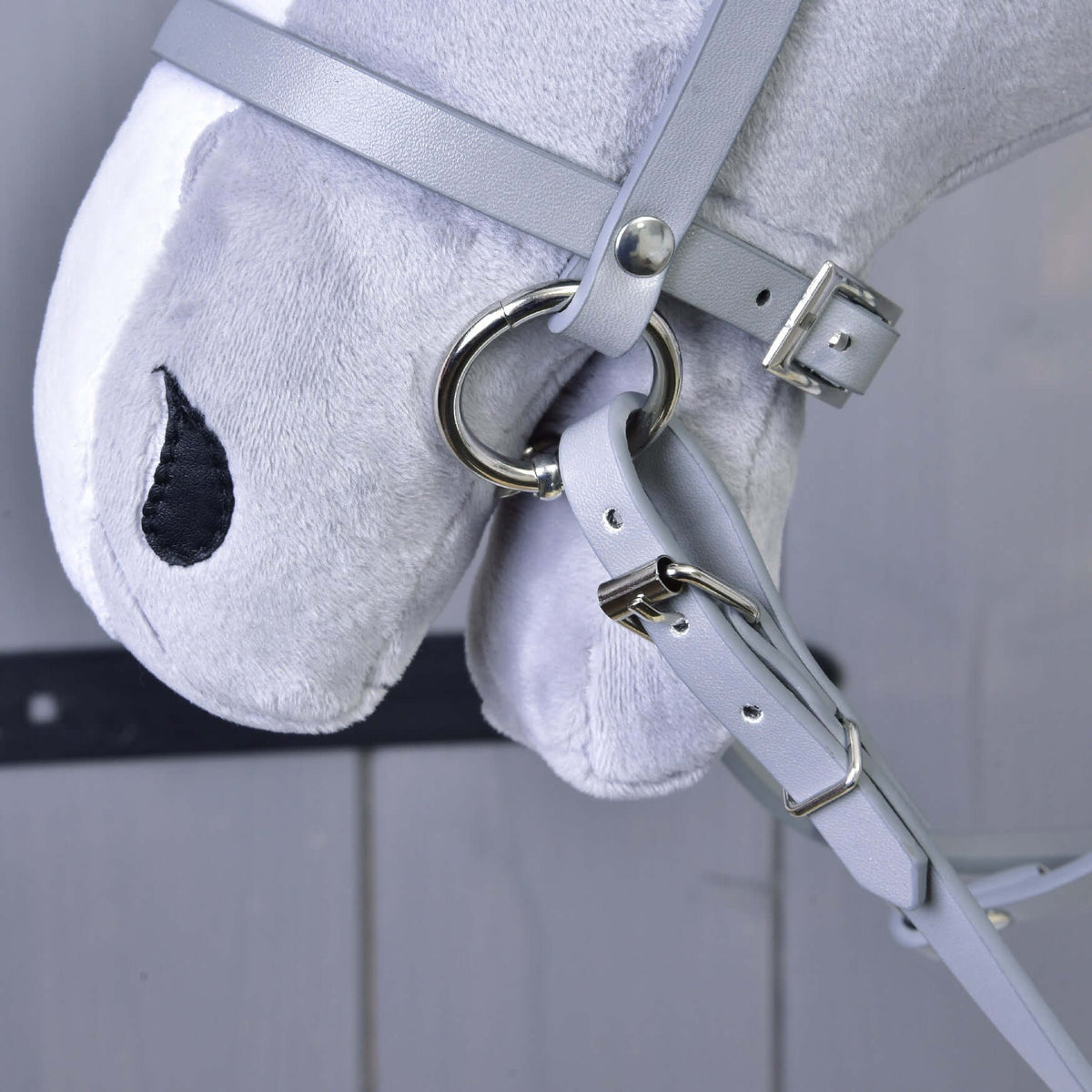 Bližnji posnetek sivega nosnika iz umetnega usnja s srebrnim obročkom in vajeti z zaponko na sivem plišastem Hobby Horse konju
