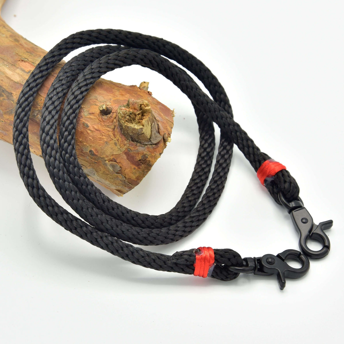 Hobby Horse Reins Spark by LarDen in black braided rope with red wraps and black snap hooks, on a branch